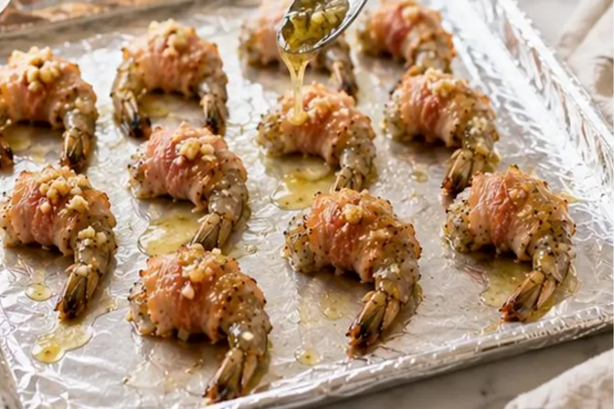 Garlic and oil mixture being spooned over bacon wrapped shrimp.