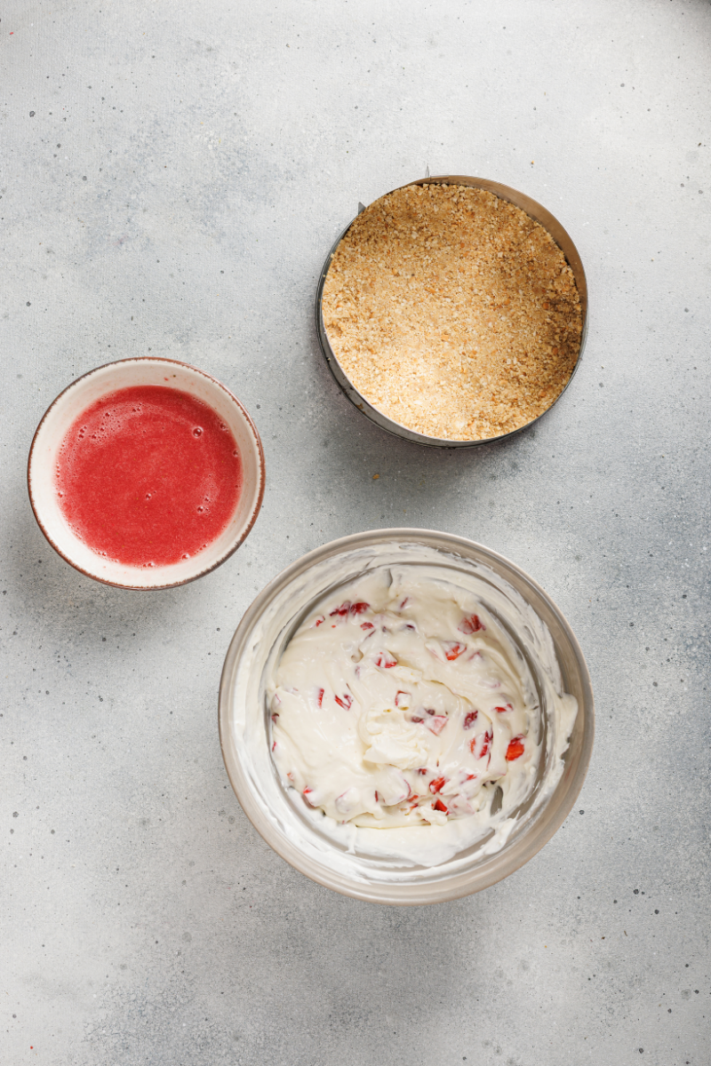 Fresh diced strawberries folded into creamy no-bake cheesecake filling with strawberry topping nearby.