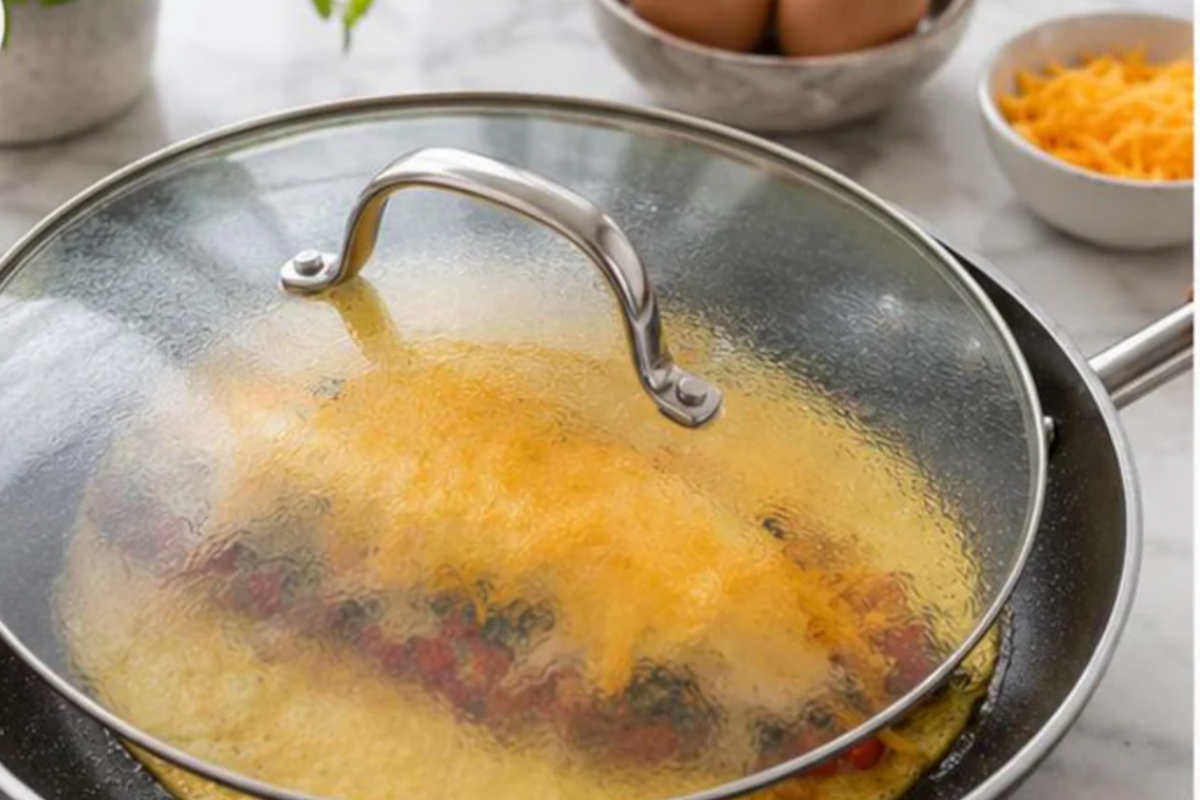 Covered skillet melting cheddar cheese over chicken and vegetable filling inside egg wrap