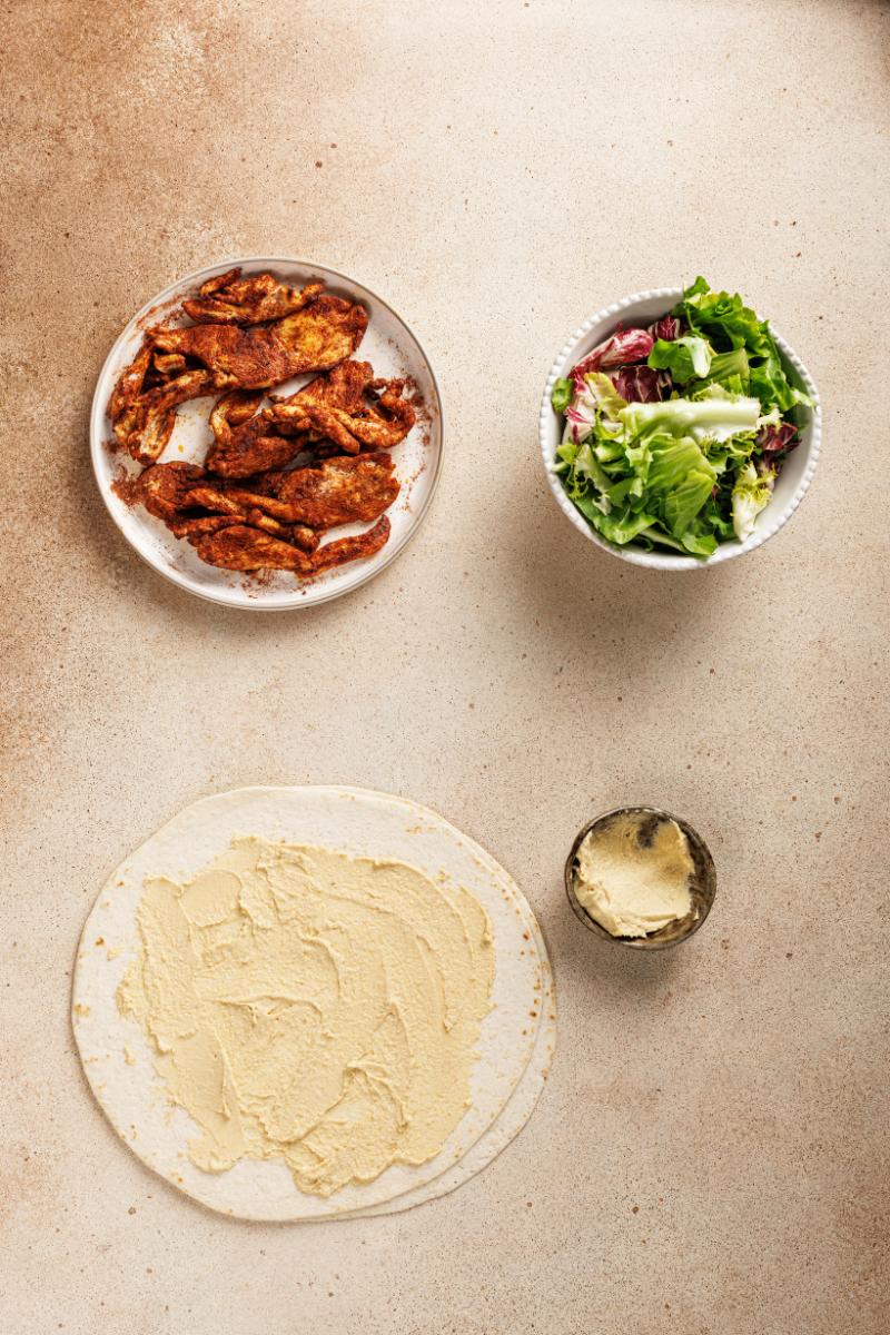 Hummus spread evenly across a large tortilla for wrap assembly