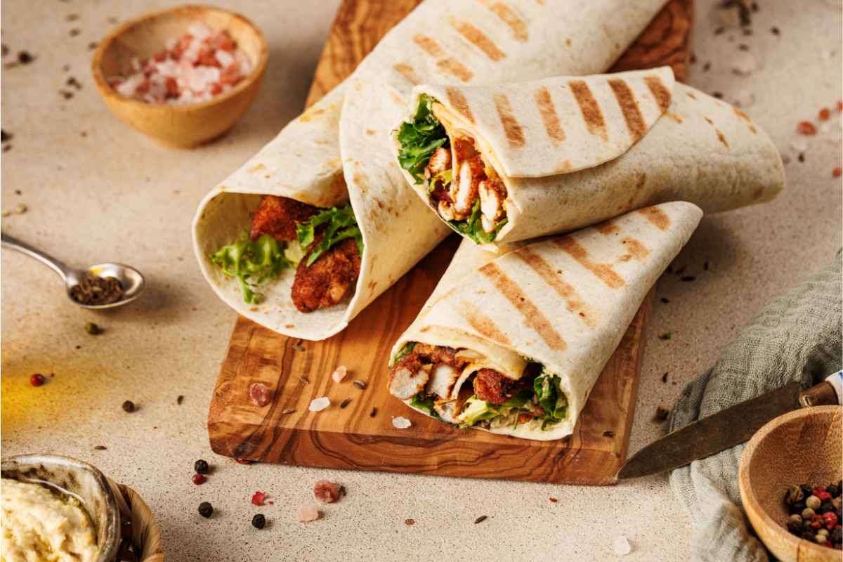 Moroccan chicken wrap cut open to show seasoned chicken, hummus and greens filling