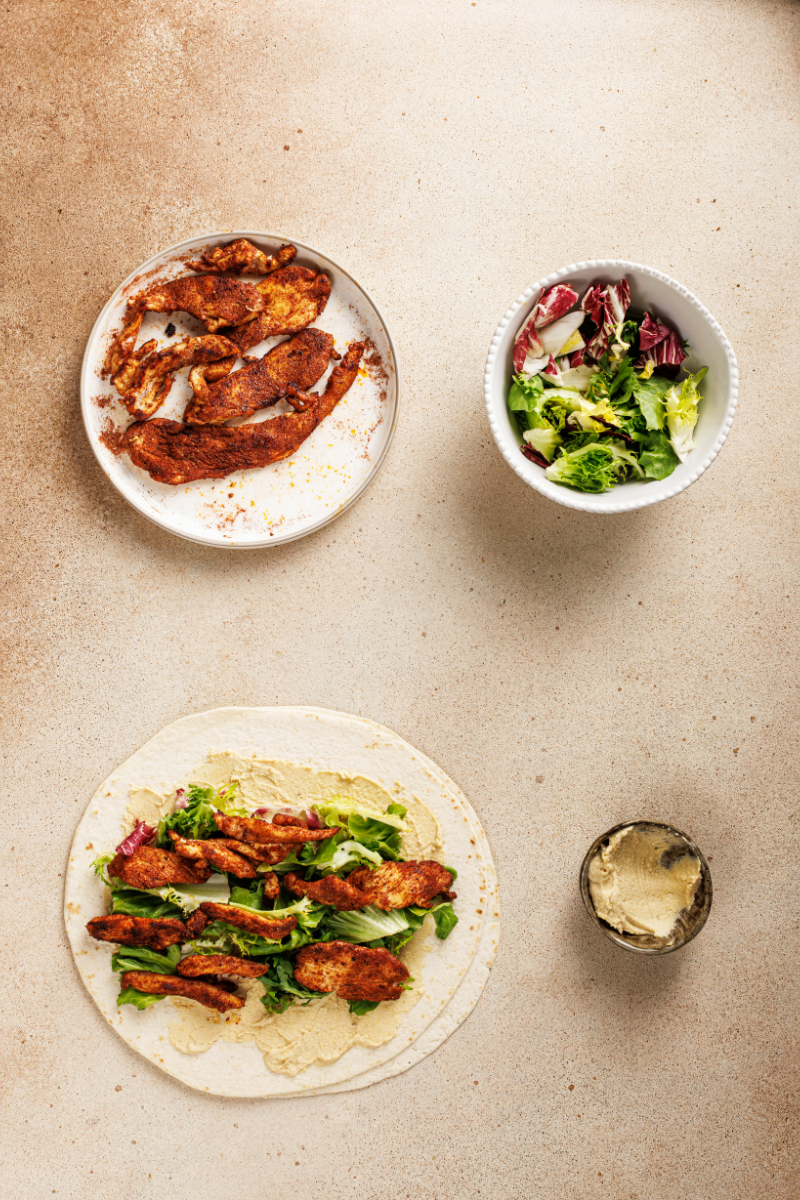 Cooked Moroccan chicken added on top of greens inside tortilla