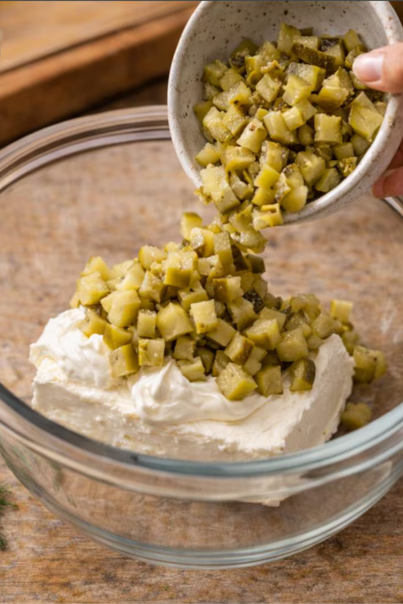 Chopped dill pickles being folded into creamy dip mixture.