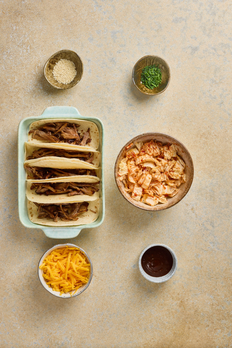  Warm tortillas standing upright in a baking dish with pulled pork added to each taco shell.