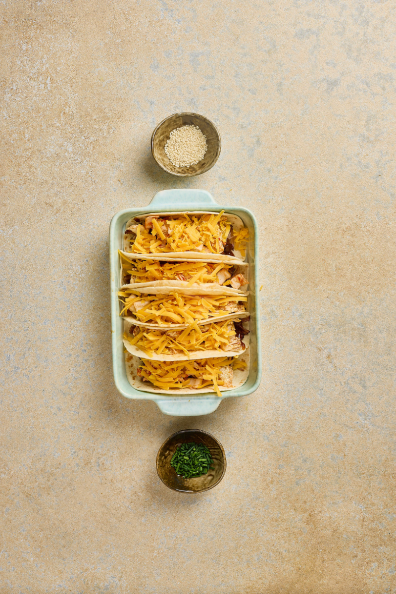 Korean BBQ pulled pork tacos topped with shredded cheddar cheese before baking.