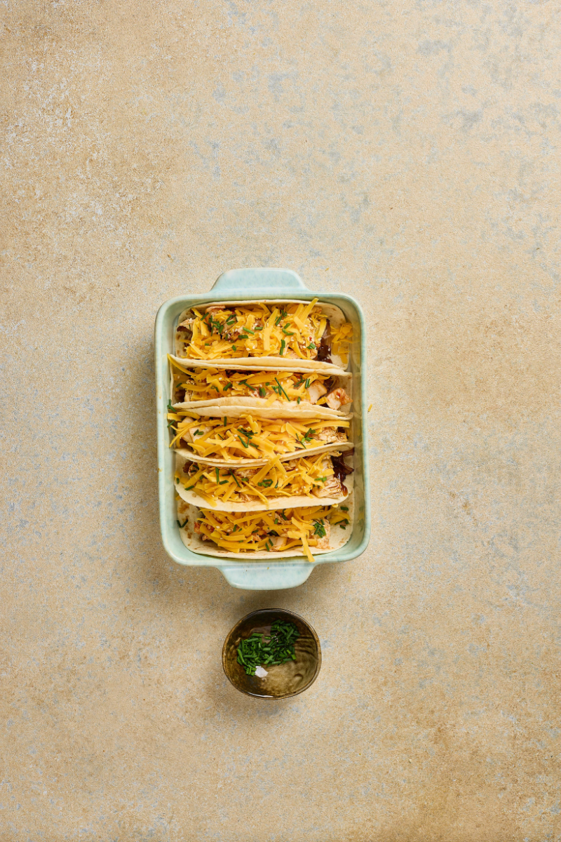 Finished Korean BBQ pulled pork tacos topped with melted cheddar cheese, sliced green onions, and sesame seeds.