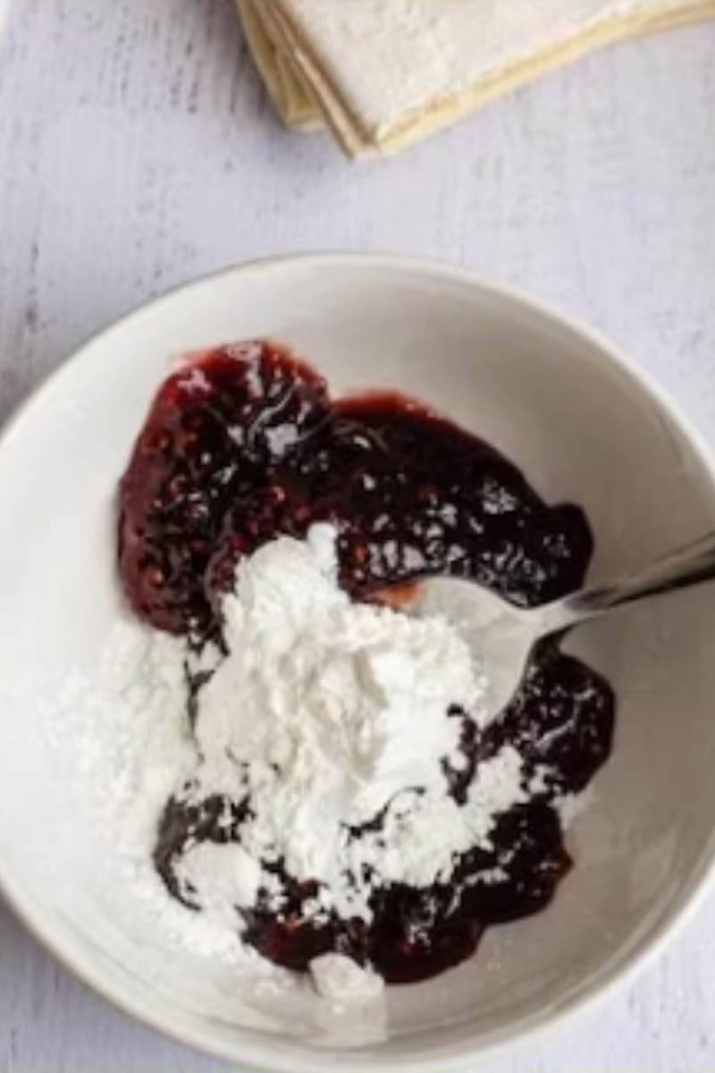 Raspberry preserves and cornstarch being mixed together in a bowl for raspberry puff pastry jam turnovers