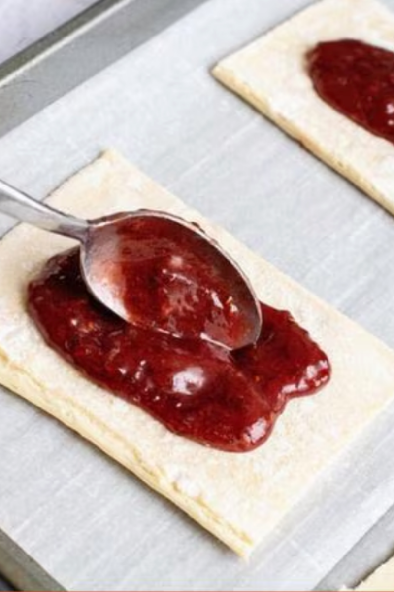 Raspberry jam filling being spooned onto puff pastry rectangles before assembling turnovers