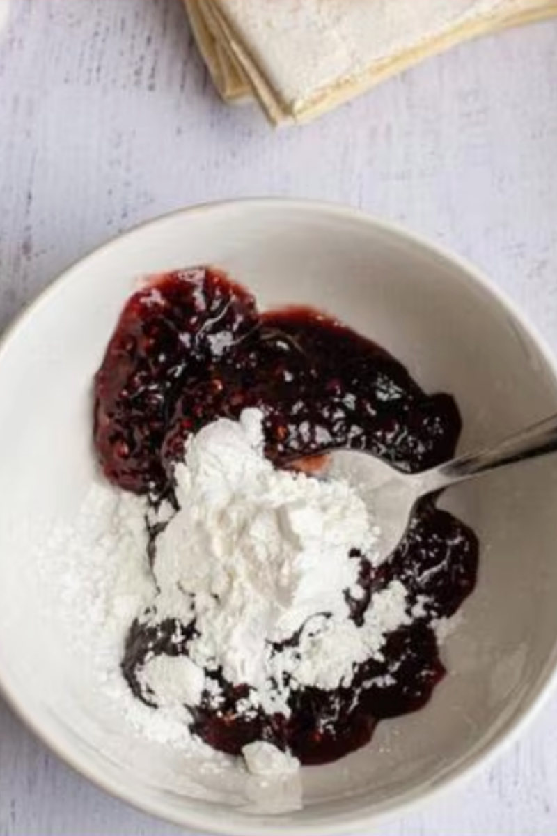 Powdered sugar being combined with raspberry preserves while preparing glaze for raspberry puff pastry turnovers