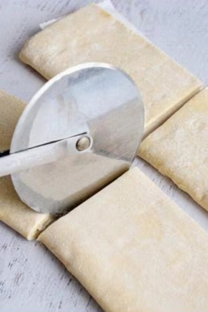 Puff pastry sheets being cut into equal rectangles for raspberry jam turnovers