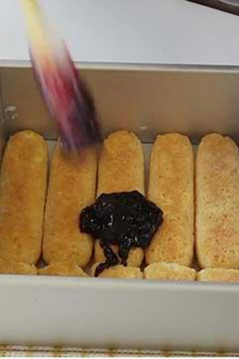 Blueberry jam spread over milk-dipped ladyfingers for the first tiramisu layer