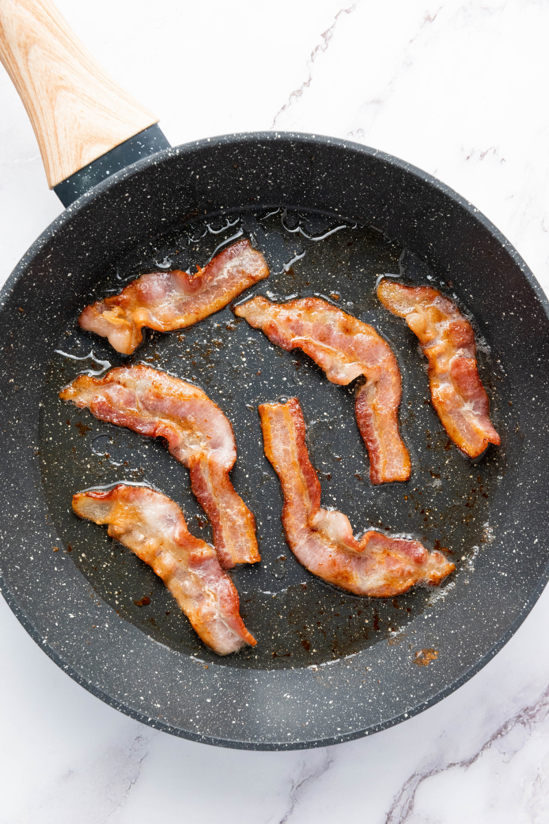 Bacon strips cooking in a skillet until crisp.