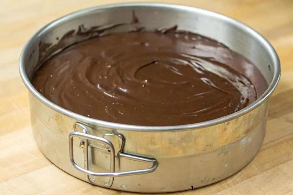 Glossy chocolate ganache spread over no-bake cheesecake in a metal springform pan.