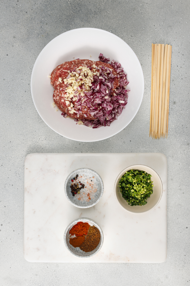 Ground meat combined with garlic, onion, herbs, and Mediterranean spices in a mixing bowl.