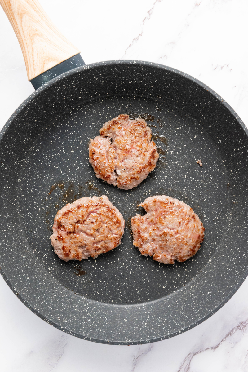 Breakfast sausage patties cooking in a skillet.