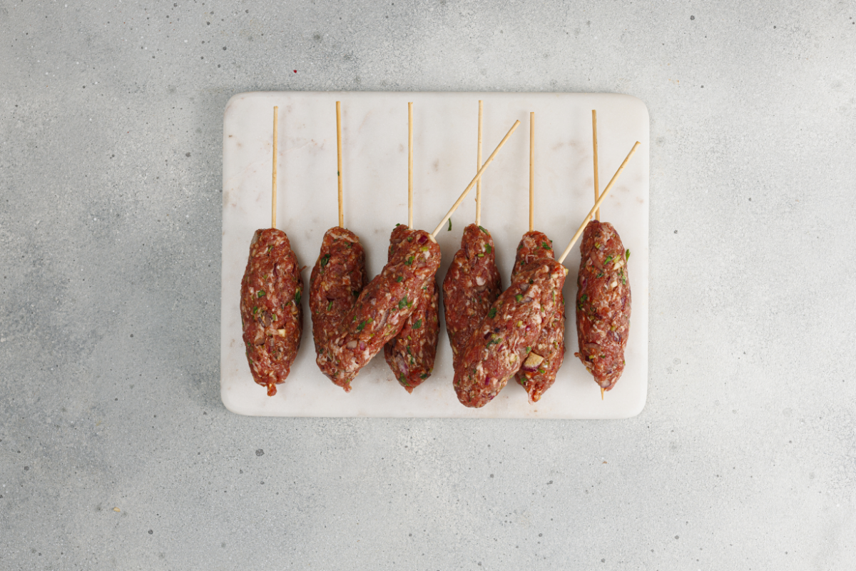Raw kofte kebabs on skewers arranged and ready for grilling.

