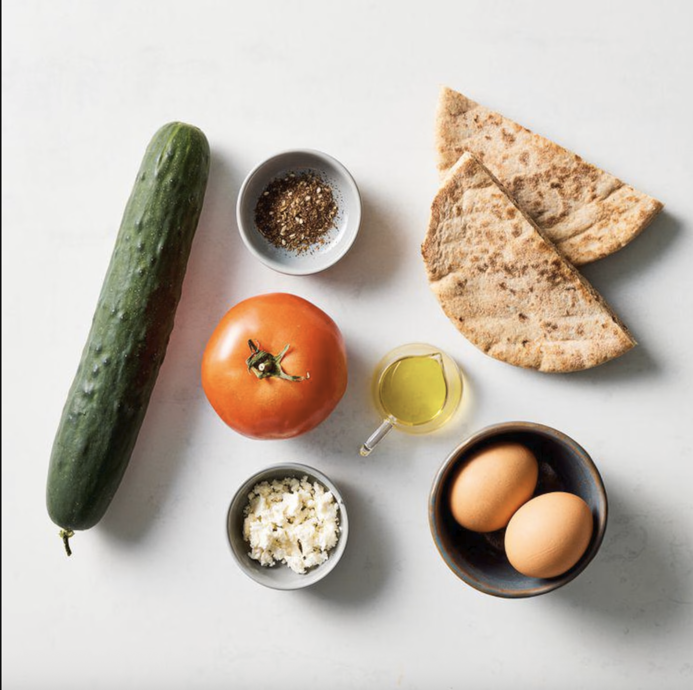 Ingredients for Egg, Tomato & Feta Breakfast Pita including whole-wheat pita, eggs, cucumber, tomato, feta cheese, olive oil, and za'atar seasoning.