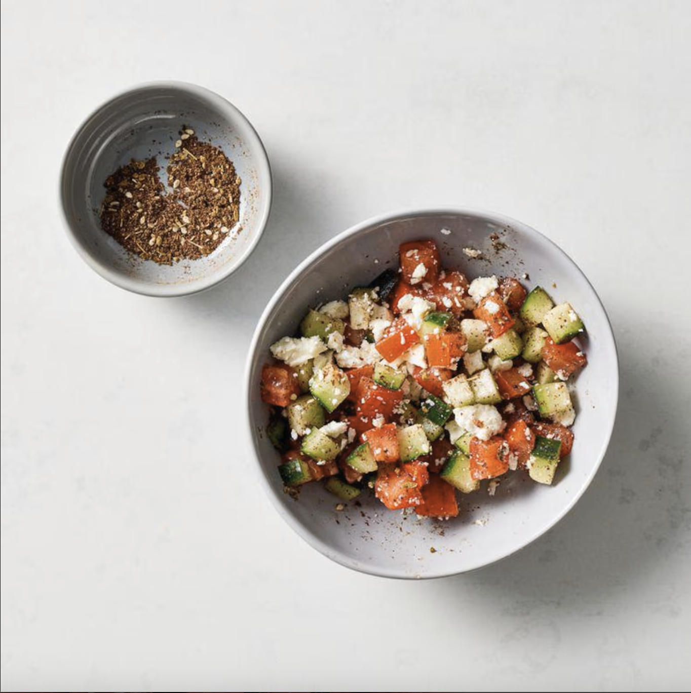 Diced cucumber, tomato, feta cheese, and za'atar tossed together in a small bowl.