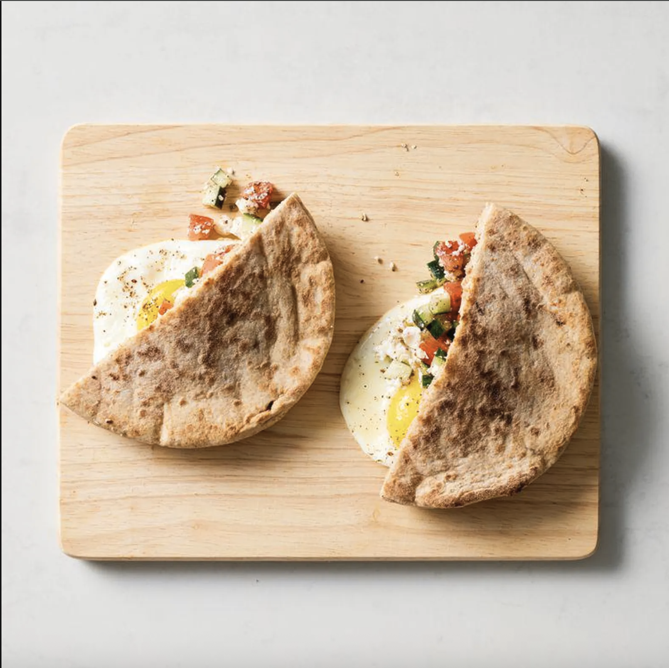 Sunny-side-up eggs tucked into warm whole-wheat pita pockets and topped with a fresh cucumber, tomato, feta, and za'atar salad before serving.