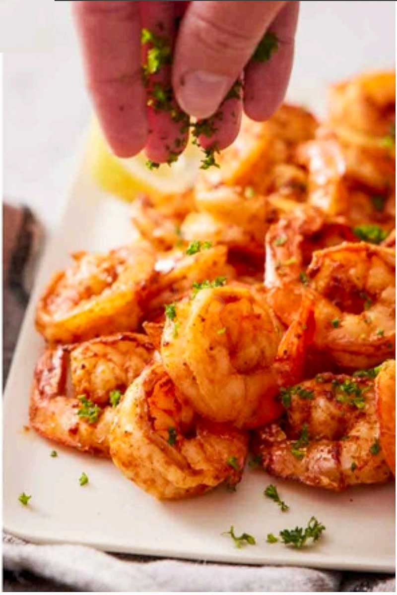 Sprinkling fresh parsley over juicy air fryer shrimp before serving with lemon wedges.