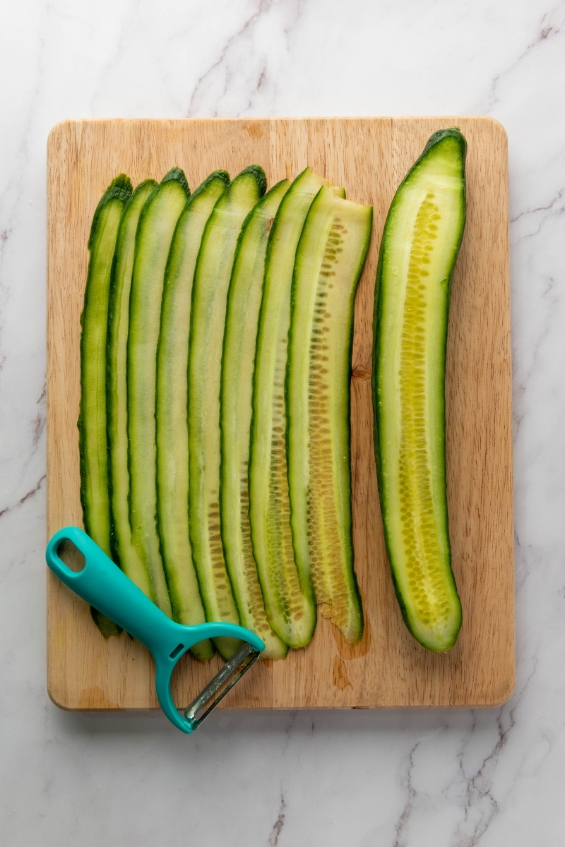 Slicing an English cucumber into thin ribbons with a vegetable peeler for Everything Bagel Cucumber Rolls.