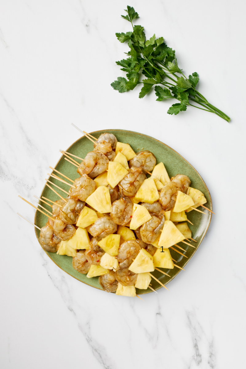 Plated grilled sweet and spicy pineapple shrimp skewers on a green plate with fresh parsley garnish