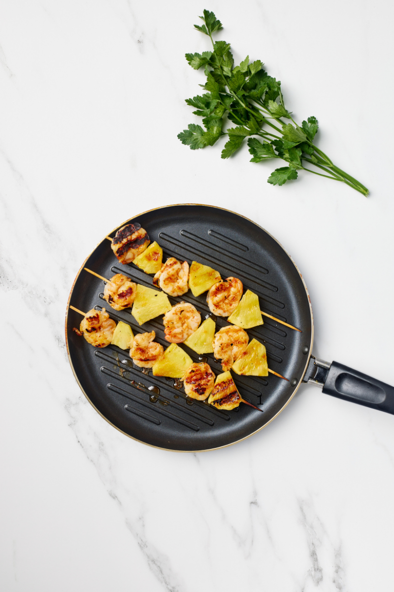 Pineapple shrimp skewers cooking on a black grill pan showing grill marks