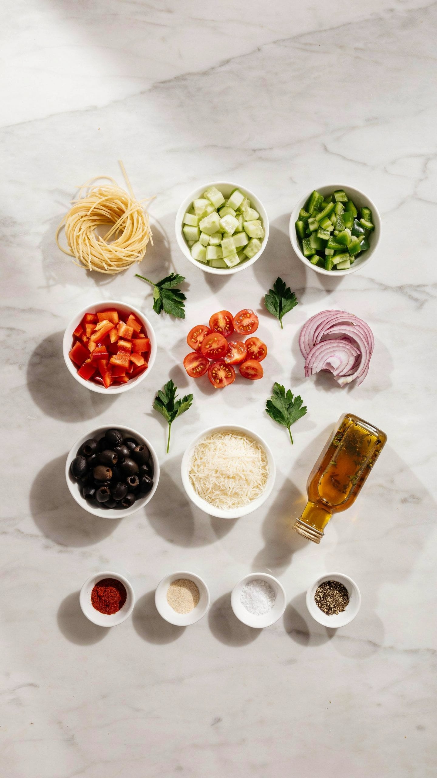 Ingredients for Spaghetti Salad including spaghetti, cucumbers, bell peppers, tomatoes, red onion, black olives, Parmesan cheese, Italian dressing, and seasonings.