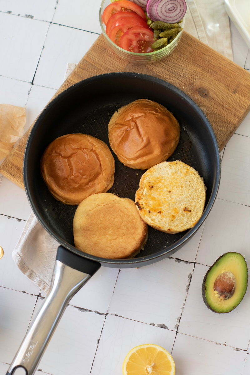 Burger buns toasting cut-side down in a skillet after cooking the halloumi cheese.

