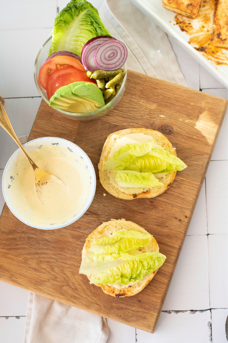 Lettuce layered onto sauce-covered toasted buns during halloumi burger assembly.

