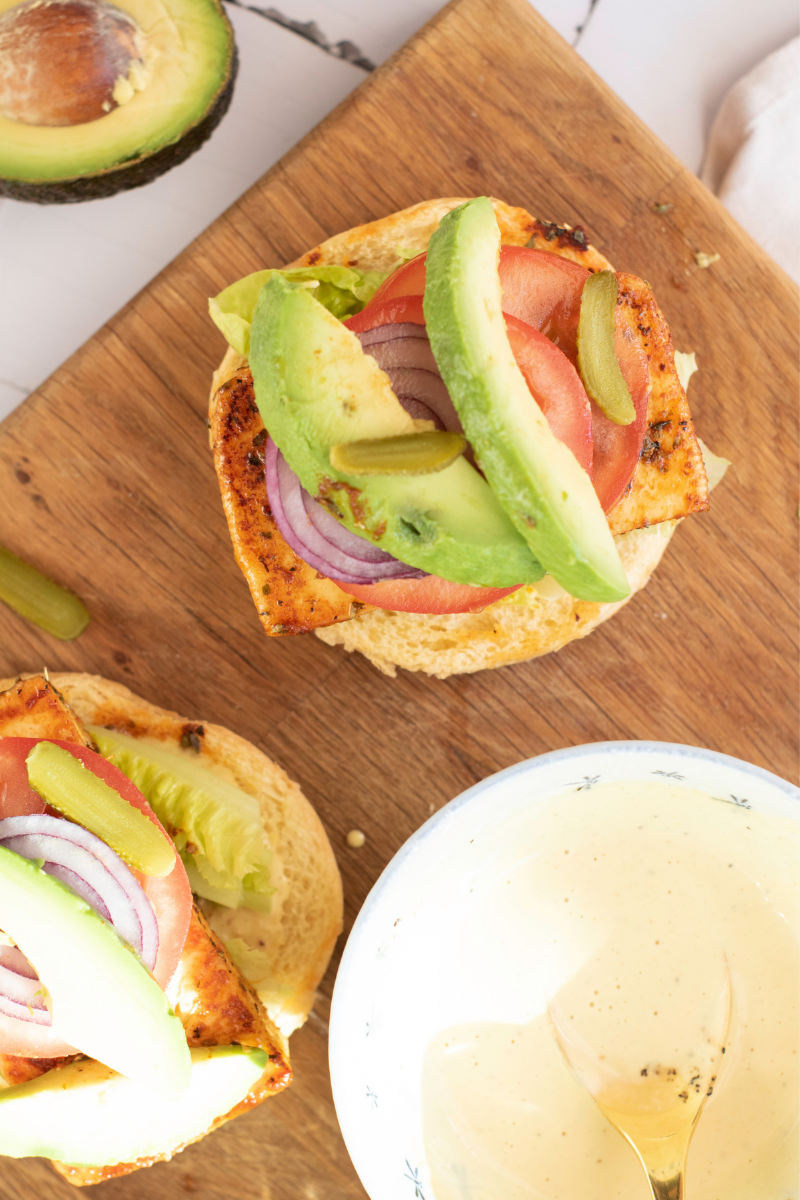 Finished halloumi burgers topped with avocado, tomato, red onion, lettuce, and creamy sauce on toasted buns.