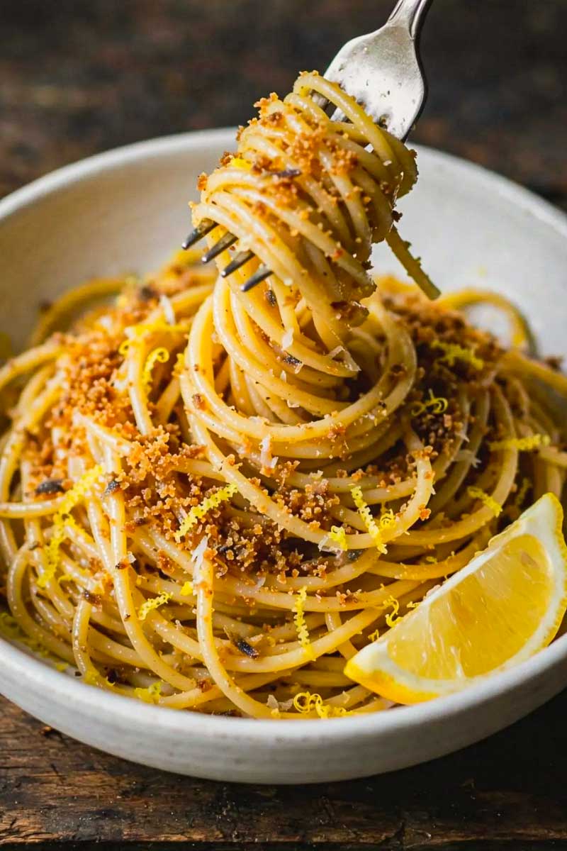 Cooked spaghetti being tossed with lemon-infused olive oil before adding freshly grated bottarga.