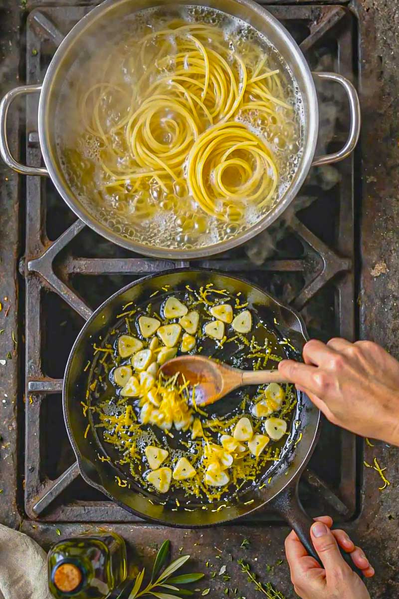 Cooked spaghetti being tossed with lemon-infused olive oil before adding freshly grated bottarga.