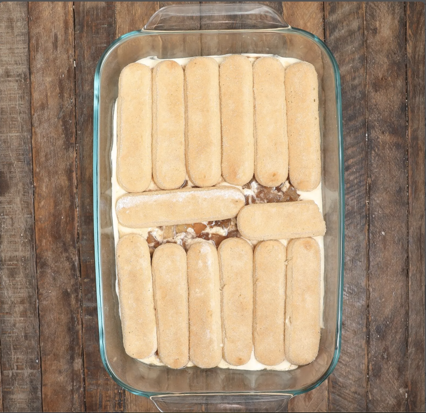 Apple-juice-dipped ladyfingers arranged snugly in a baking dish for Caramel Apple Tiramisu.