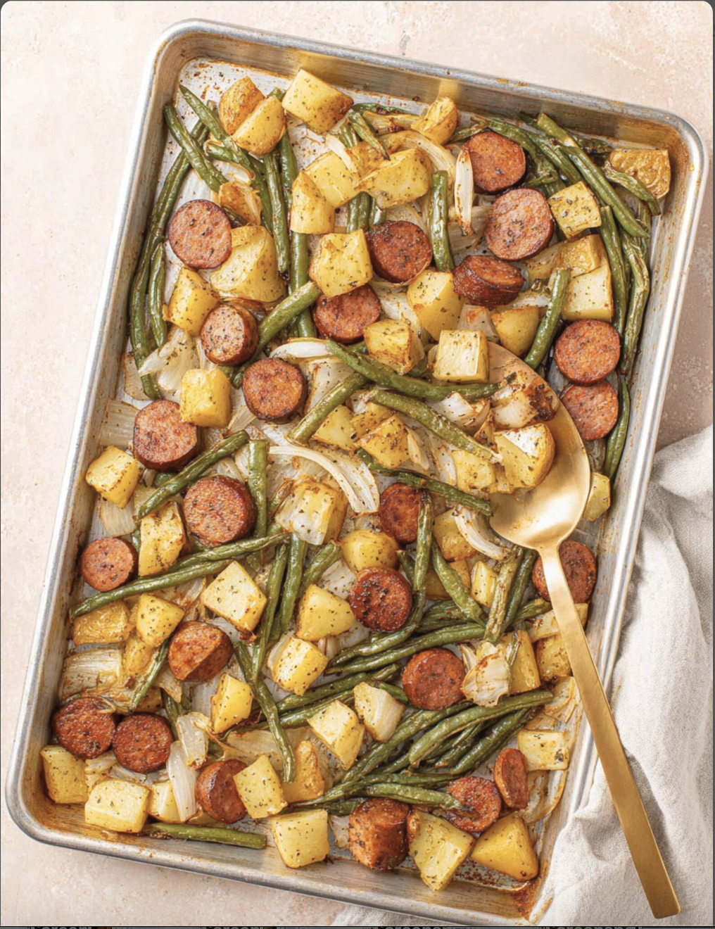 Sheet pan sausage, roasted potatoes, green beans and onion with a serving spoon.