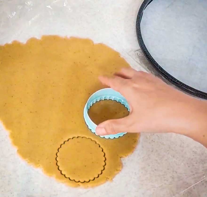 Rolled baklava cookie dough being cut into individual round cookies with a cookie cutter.