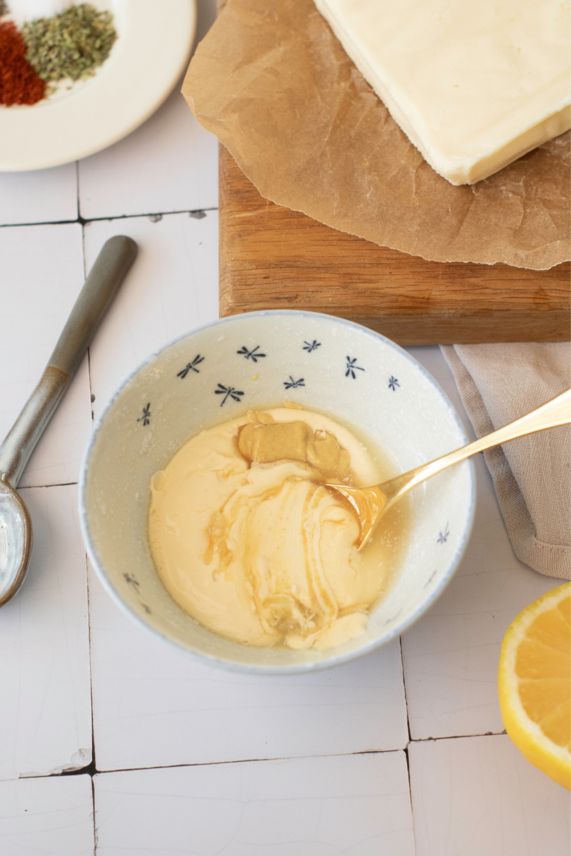 Creamy lemon Dijon burger sauce being mixed in a bowl beside burger buns and fresh lemon.