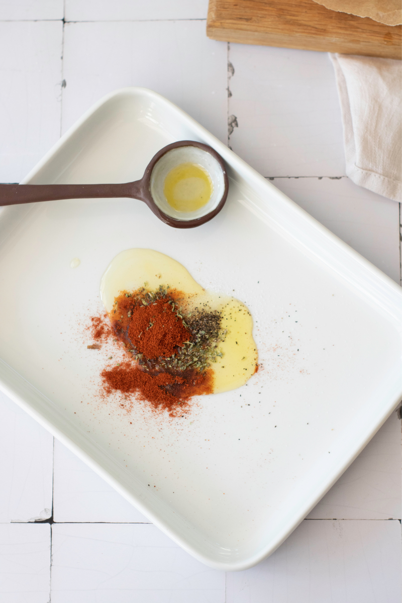 Olive oil, paprika, oregano, salt, and pepper prepared on a plate for seasoning halloumi cheese.