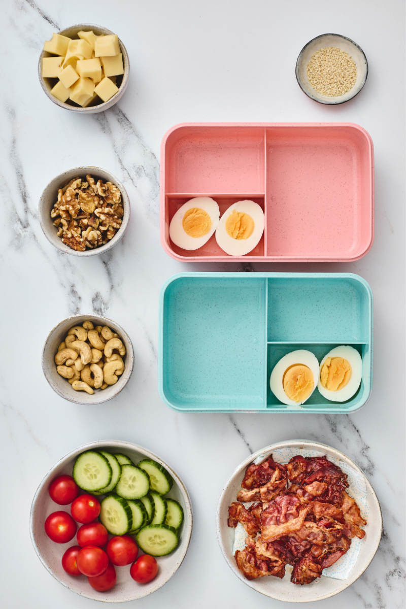 Hard-boiled egg halves placed into two colorful compartment lunchboxes.

