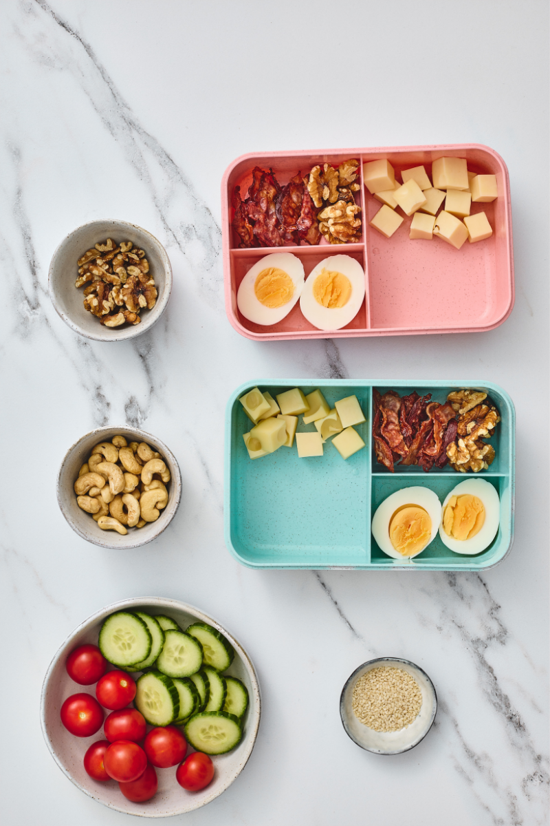 Cheese cubes added to lunchboxes with hard-boiled eggs, crispy bacon, and walnuts.