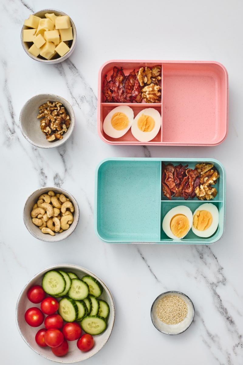Walnuts added beside crispy bacon and hard-boiled eggs in two protein lunchboxes.