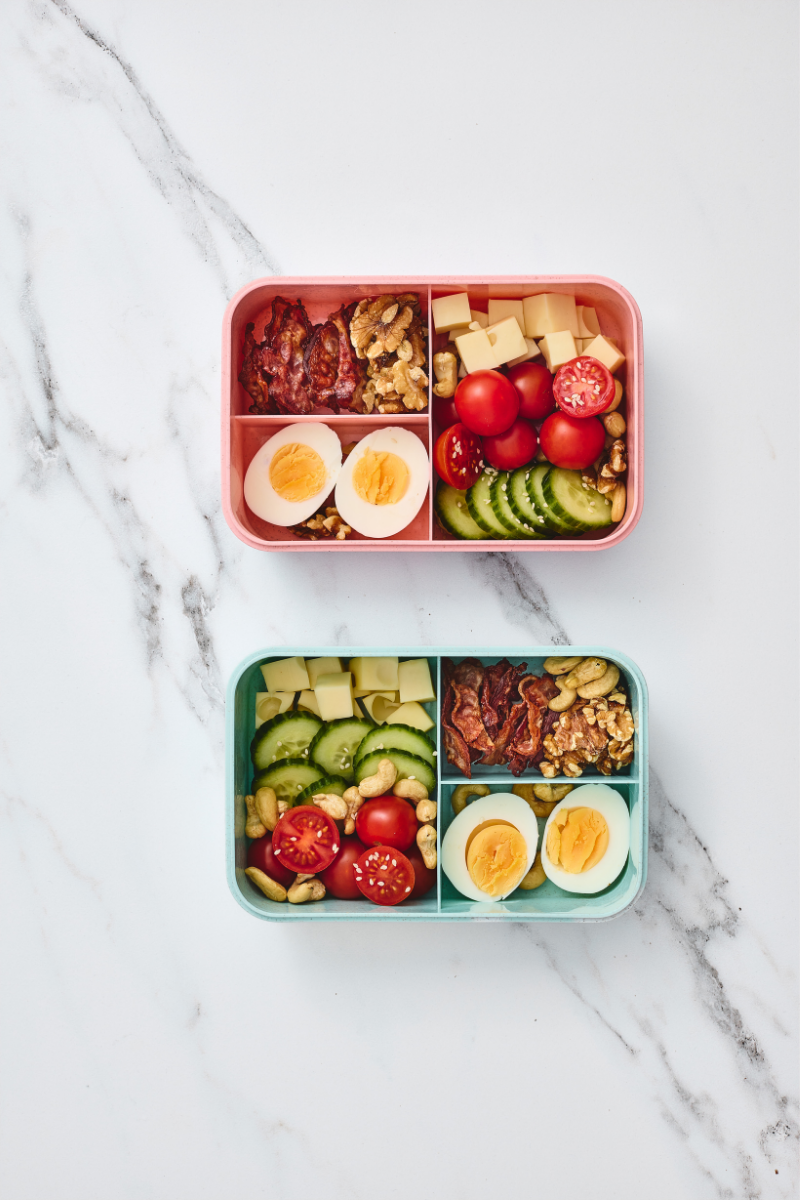  Completed savory protein lunchboxes with eggs, bacon, cheese, walnuts, cashews, cucumber, cherry tomatoes, and sesame seeds.
