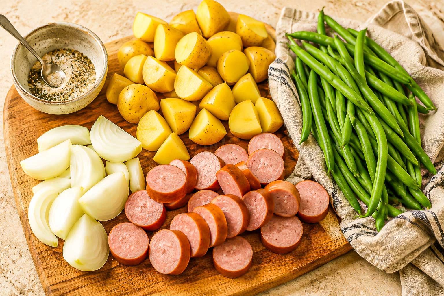 Cut potatoes, sliced sausage, onion wedges, green beans and seasoning prepared for roasting.