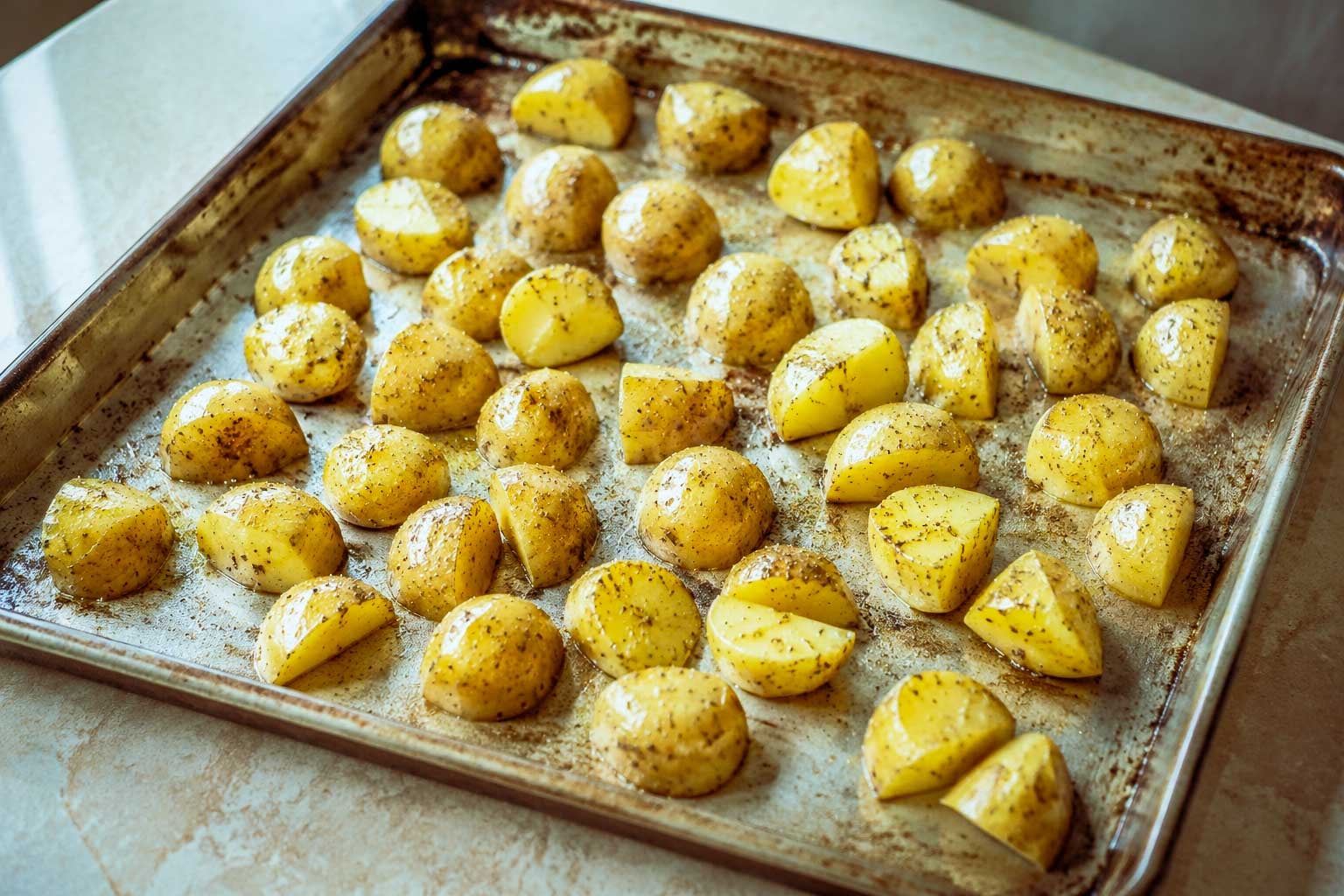 Seasoned baby potatoes spread in a single layer on a metal sheet pan.