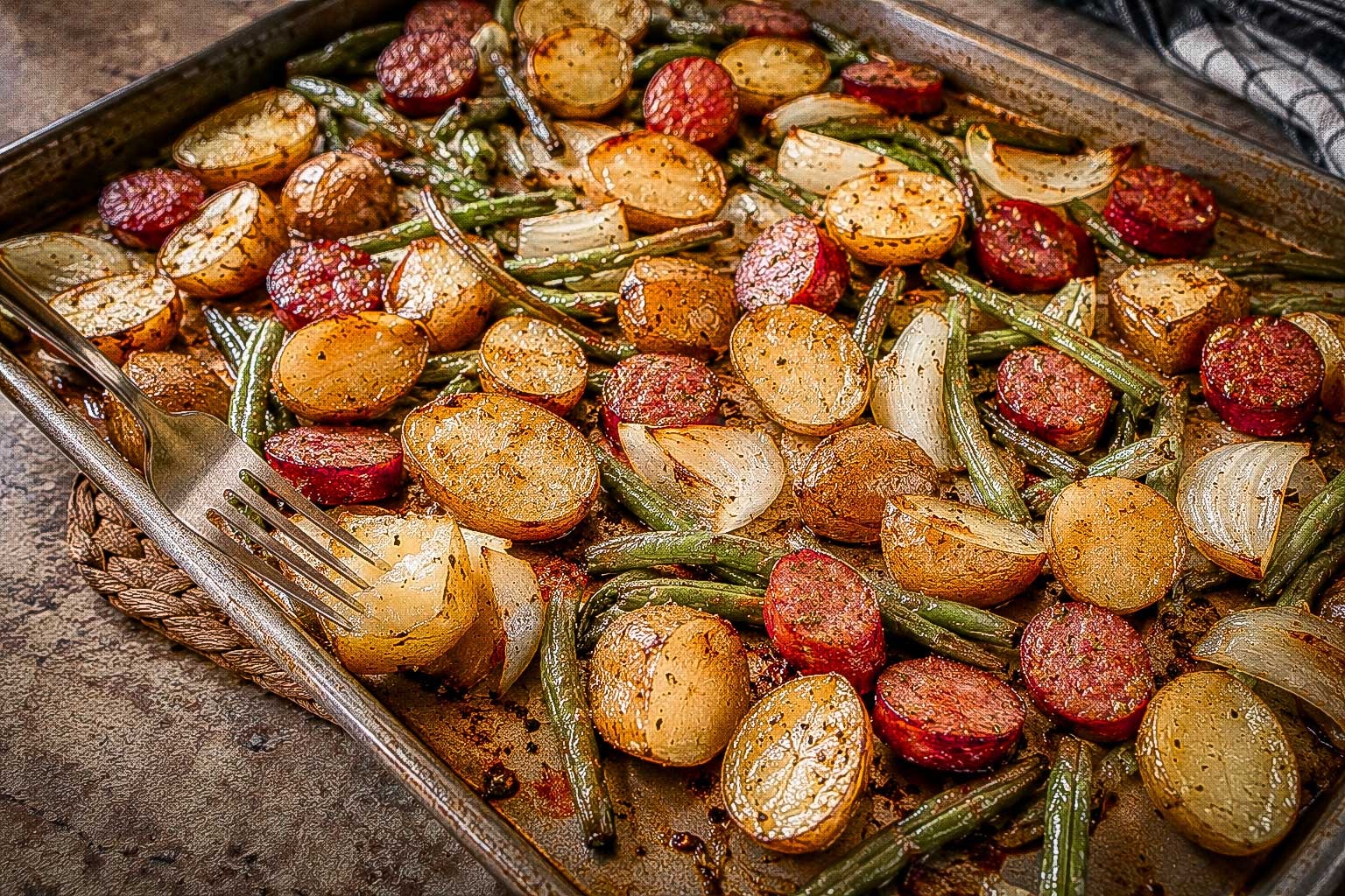 Sliced sausage, potatoes, green beans and onion arranged on a sheet pan