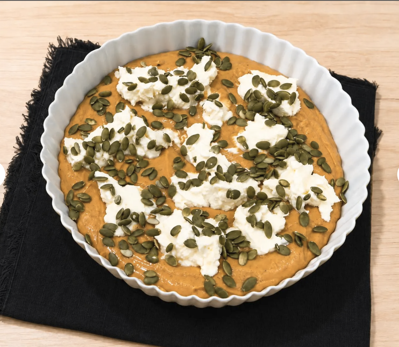 Unbaked pumpkin cream cheese cake topped with cream cheese and pumpkin seeds.

