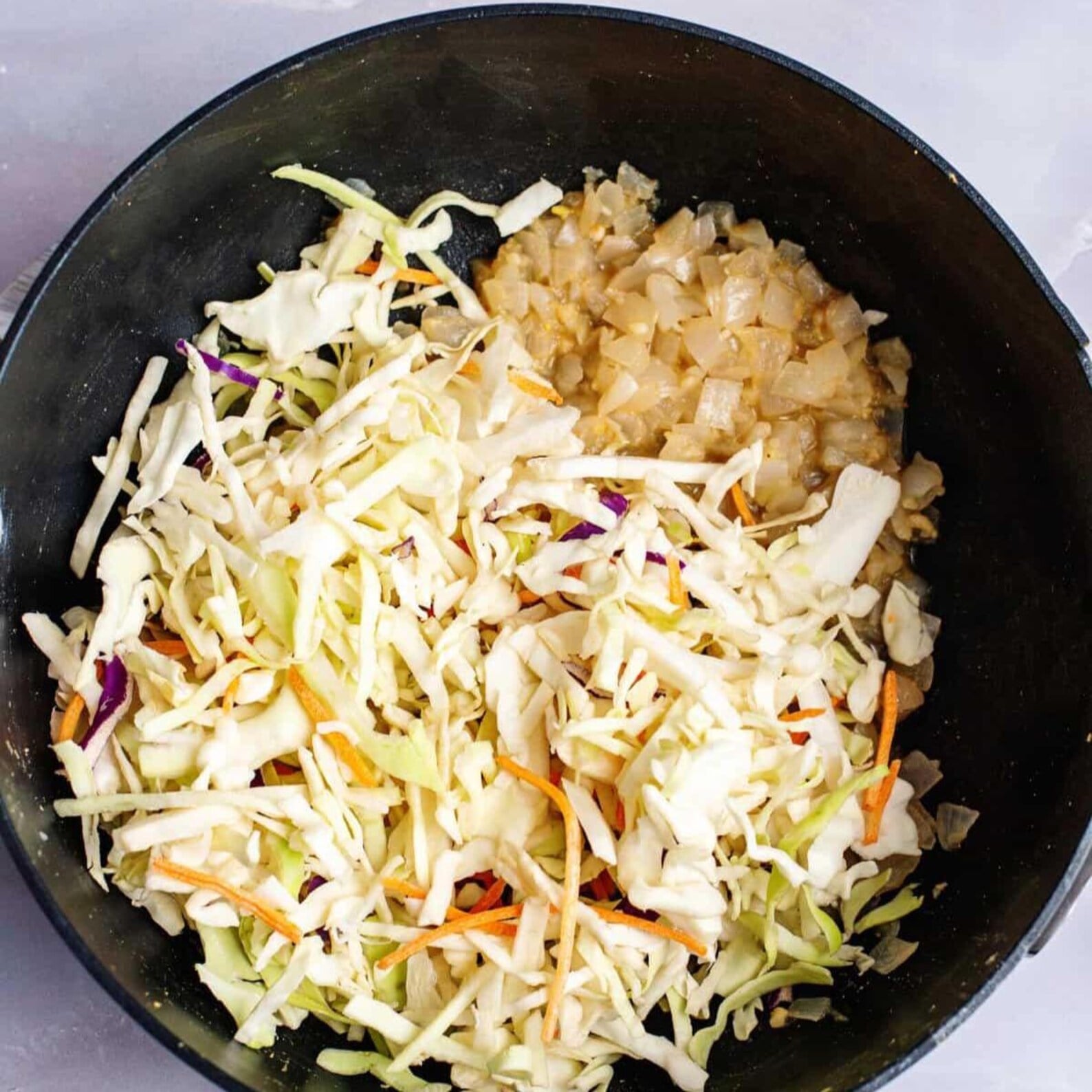 Shredded cabbage and carrot coleslaw mix cooking with onions in a skillet for Egg Roll in a Bowl.