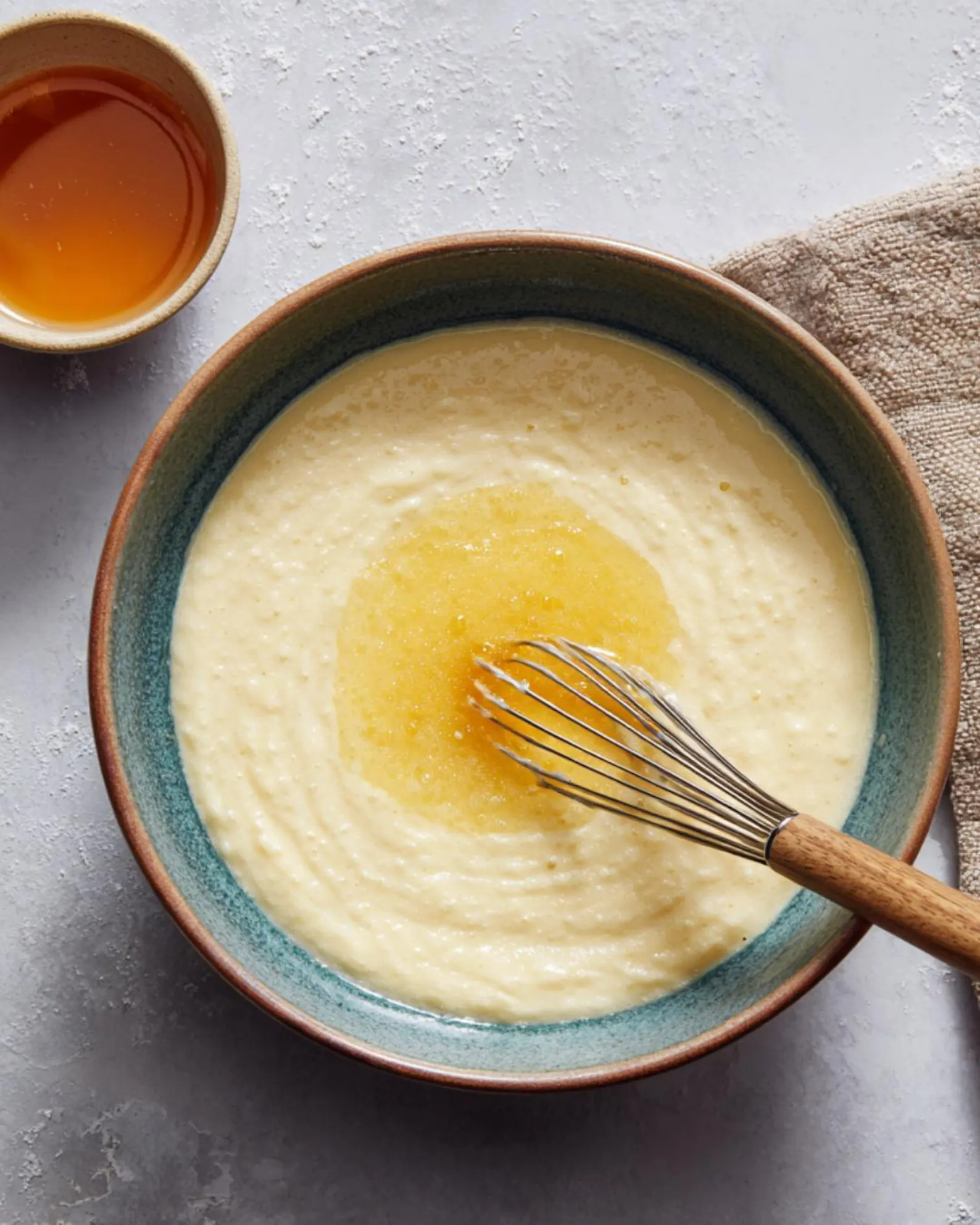 Egg, milk and vanilla being whisked together in a ceramic bowl for mini cinnamon apple fritter batter.