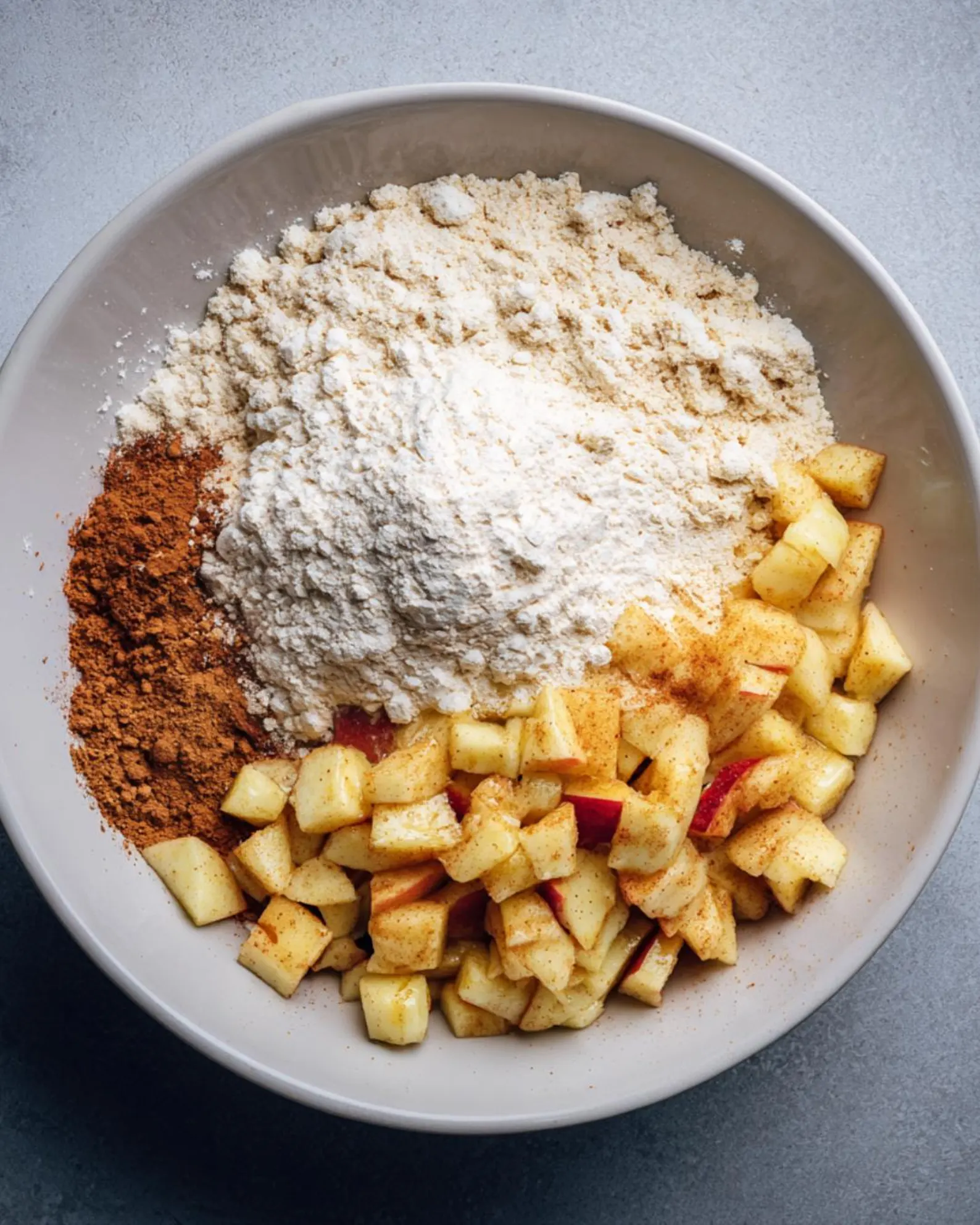 Diced apples with flour, cinnamon, nutmeg, sugar, baking powder and salt in a mixing bowl for mini apple fritters.