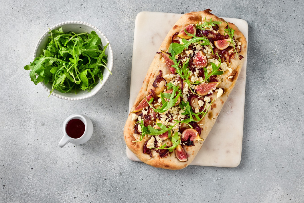 Finished fig and caramelized onion flatbread topped with fresh arugula, sliced figs, red onions, and crumbled white cheese.